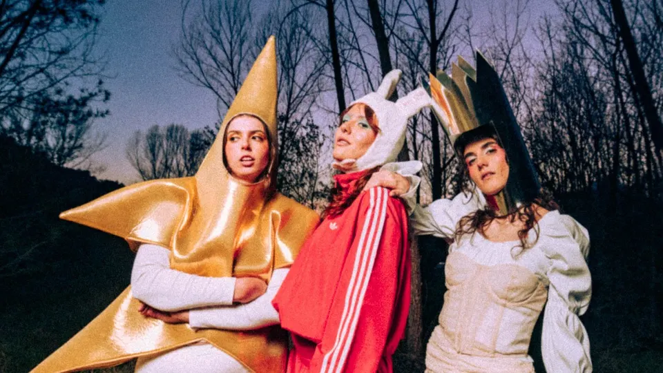 Las tres integrantes de La 126 posan disfrazadas en un bosque al anochecer: una con un traje de estrella dorada, otra con chándal rojo y gorro de conejo y la tercera con un vestido blanco y una corona