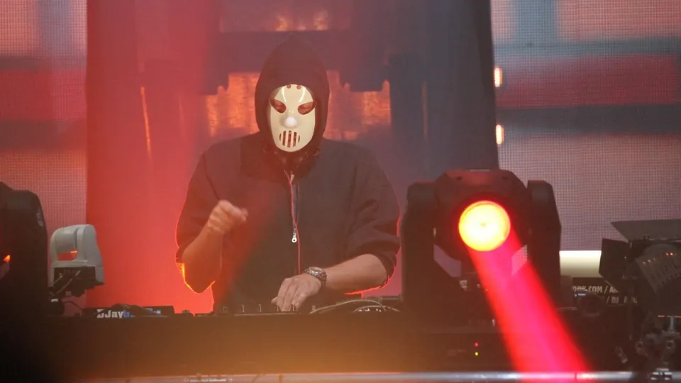 Angerfist, con capucha y su máscara blanca, pincha en una cabina iluminada con focos rojos