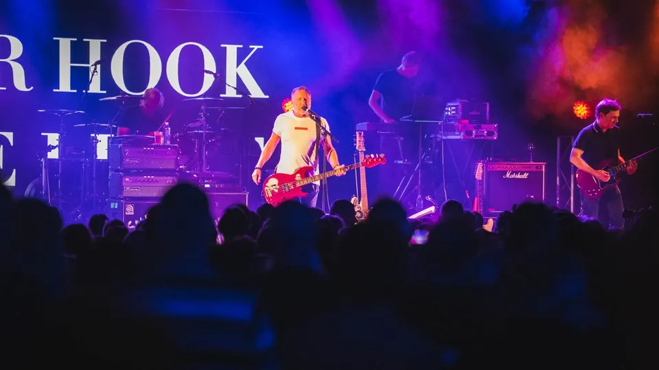 Peter Hook canta y toca un bajo rojo en el centro del escenario junto a The Light, bajo luces moradas y con el público en primer término, en el festival Rockaway Beach de 2023