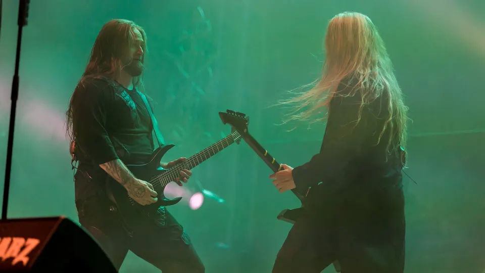 Dos guitarristas de Hypocrisy de pelo largo tocan frente a frente sobre un escenario bañado en luz verde y humo, durante su concierto en el festival Rockharz de 2024