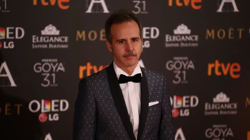 Marc Crehuet, con bigote, esmoquin estampado azul oscuro y pajarita negra, posa en el photocall de los Premios Goya de 2017 ante un fondo con logotipos