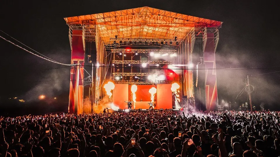 Escenario principal de Extremúsika 2023 en Cáceres de noche, con llamaradas sobre el escenario iluminado en naranja y miles de personas con los brazos en alto en primer plano