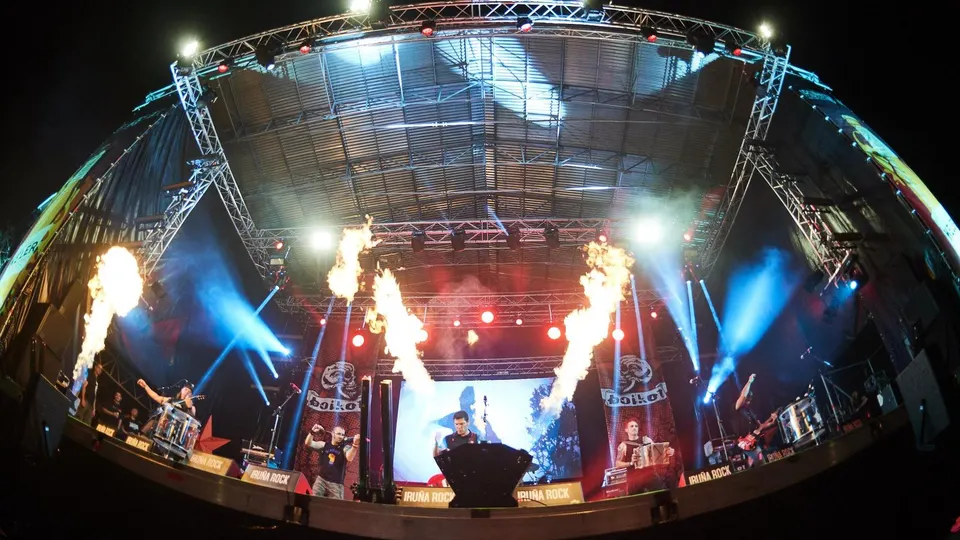 Boikot tocan en un gran escenario al aire libre con columnas de fuego, focos azules y pancartas con el logotipo del grupo, en una foto tomada con objetivo de ojo de pez