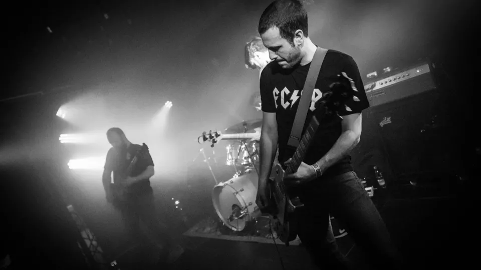 Concierto de Toundra en blanco y negro: un guitarrista con camiseta oscura toca en primer plano y otro músico se recorta a contraluz junto a la batería