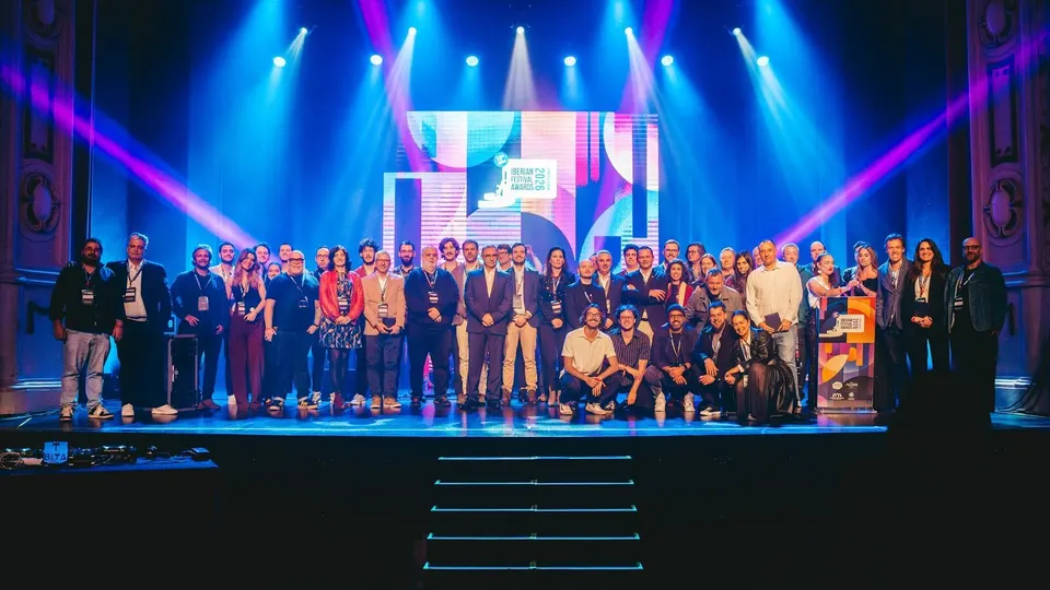 Decenas de asistentes posan en grupo sobre el escenario del Coliseu Micaelense, bajo focos azules y morados, con el logotipo de los Iberian Festival Awards 2026 en la pantalla del fondo
