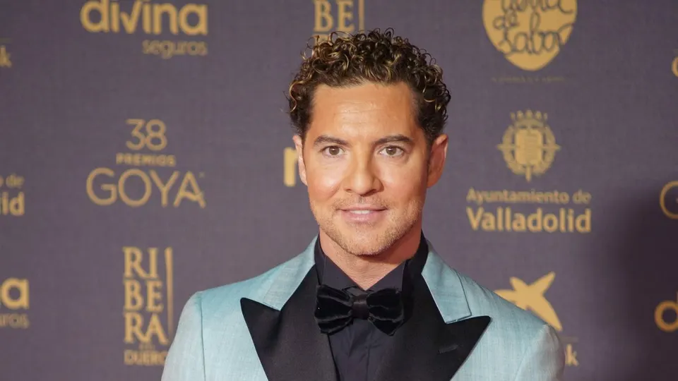 David Bisbal sonríe en la alfombra roja de los Premios Goya 2024, con chaqueta azul celeste de solapas negras y pajarita negra, ante un photocall con logotipos dorados