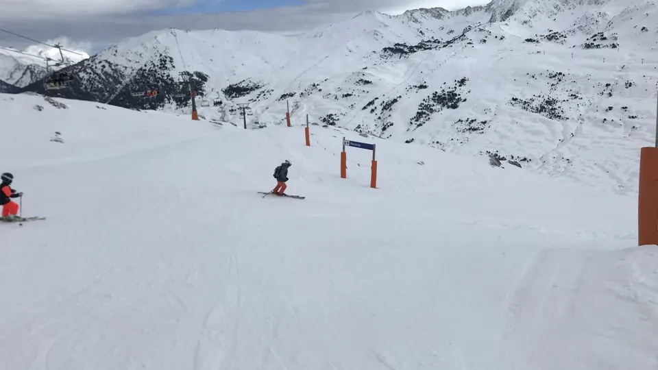 Dos esquiadores bajan por una pista nevada de Baqueira Beret, con un telesilla a la izquierda y montañas cubiertas de nieve al fondo