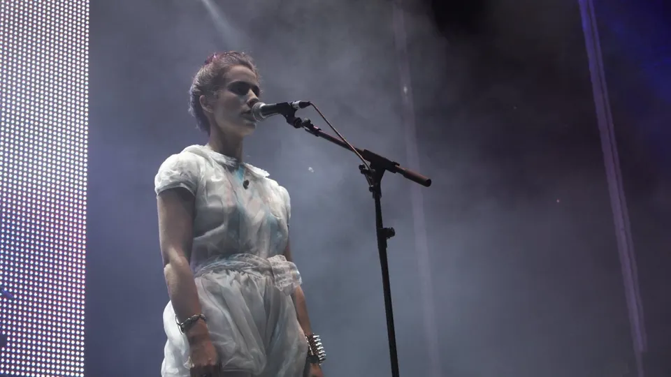 Ariadna Paniagua, cantante de Los Punsetes, de pie e inmóvil ante el micrófono con un vestido blanco y humo en el escenario
