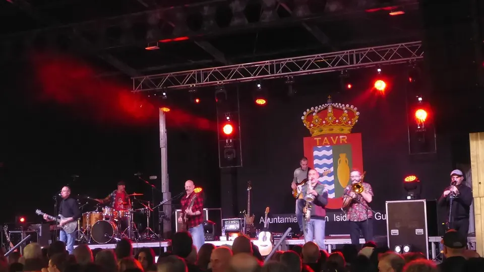 Celtas Cortos tocan en un escenario con luces rojas, con guitarras, saxofón, trombón y flauta, ante el público