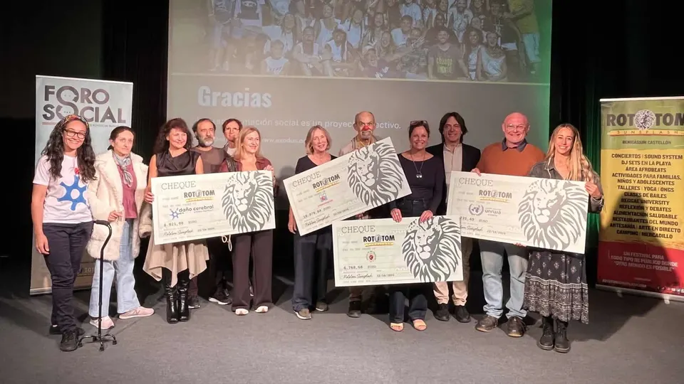 Representantes de Rototom Sunsplash, la Fundación Exodus y las cuatro entidades beneficiarias posan en un escenario del EACC de Castelló con cheques gigantes, uno de ellos sostenido por un payaso de Payasospital, ante una pantalla con la palabra Gracias