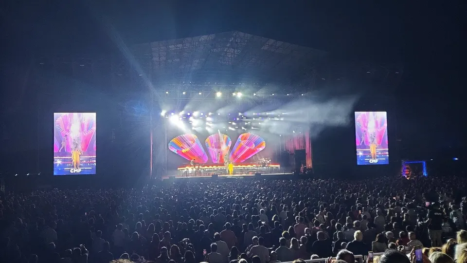 Público abarrotando la explanada del Concert Music Festival de Sancti Petri durante un concierto nocturno de julio de 2025, frente al escenario iluminado con focos, una escenografía de colores y dos pantallas laterales con el logotipo CMF