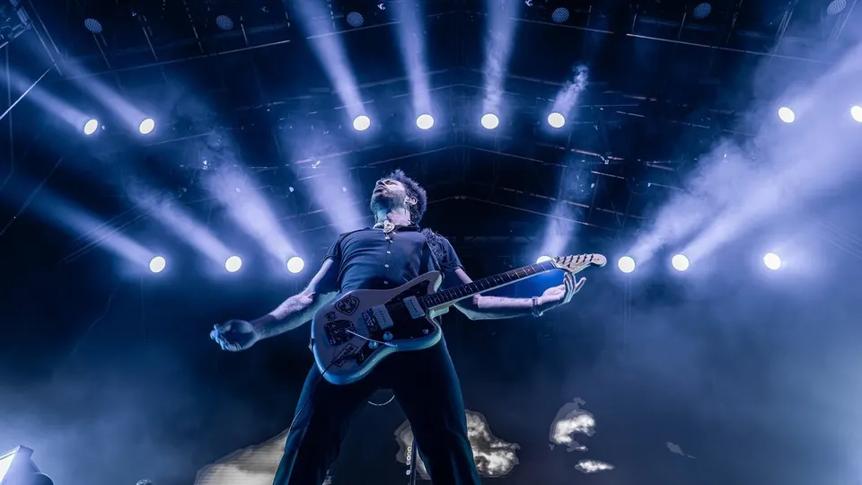Un guitarrista de Viva Suecia, con la cabeza alzada y la guitarra en las manos, bajo una fila de focos azules en el escenario de Brisa Festival 2025