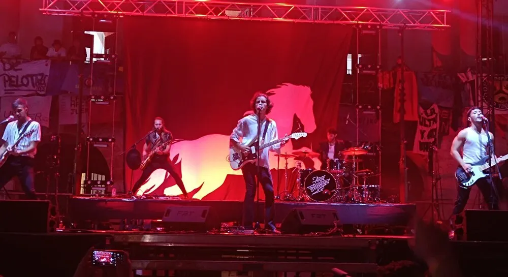 Arde Bogotá tocan en un escenario bañado de luz roja, con la silueta de un caballo proyectada al fondo y los cuatro músicos con guitarras y batería