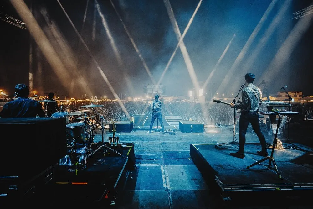 Vista desde el fondo del escenario de Arenal Sound durante un concierto de Dorian, con el cantante frente a una multitud iluminada por focos blancos
