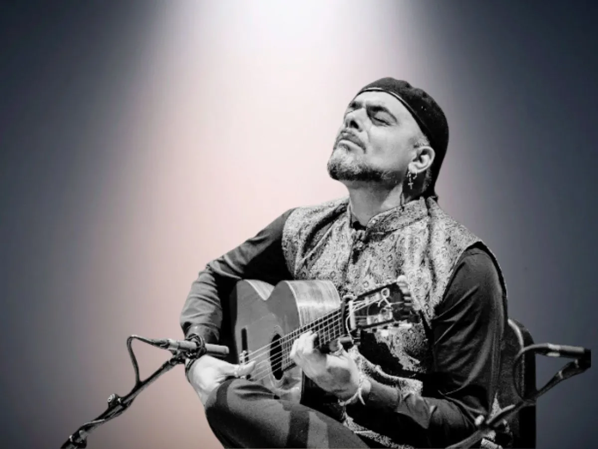 El guitarrista Jerónimo Maya, con boina y chaleco estampado, toca sentado frente a dos micrófonos con los ojos cerrados y la cabeza echada hacia atrás, en una imagen en blanco y negro