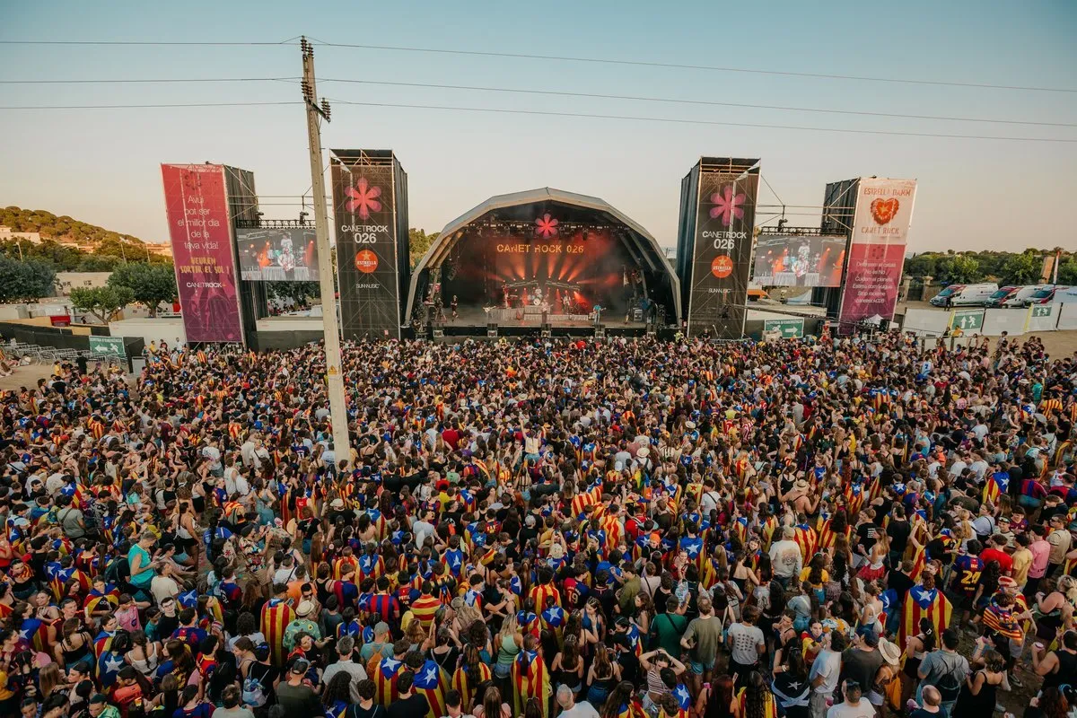 Vista desde lo alto del público llenando el Pla d'en Sala ante el escenario de Canet Rock 2026 al atardecer, con muchas esteladas y senyeres y las pantallas laterales del festival