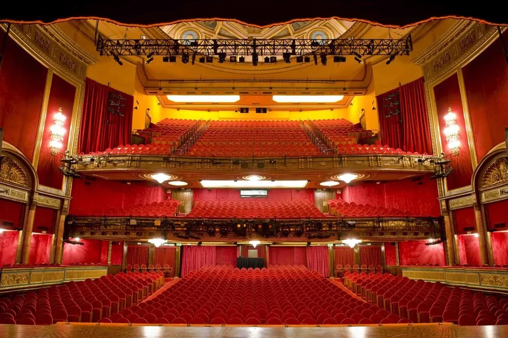 Patio de butacas del Teatro Lope de Vega de Madrid, con butacas rojas, dos pisos de palcos y el telón rojo cerrado