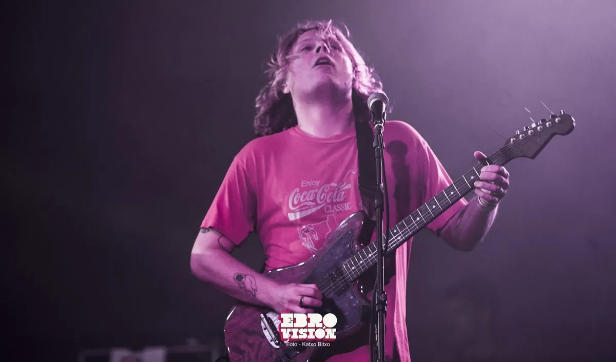 Ty Segall canta con los ojos cerrados y la cabeza hacia atrás mientras toca una guitarra eléctrica, con camiseta rosa y bajo una luz morada, en un concierto de Ebrovisión