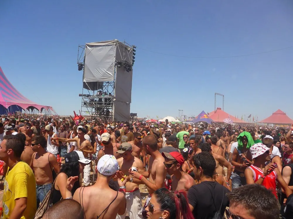 Público de Monegros Desert Festival a pleno sol en el desierto de Fraga, con una torre de sonido y carpas rojas, rosas y azules al fondo