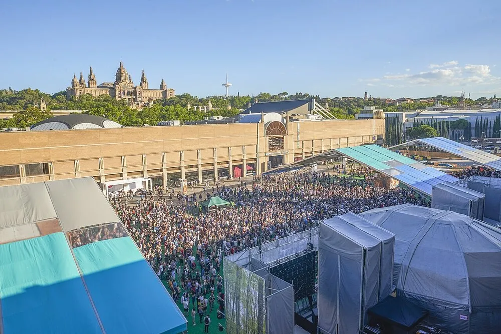 Vista elevada del público del Sónar by Day 2016 en Barcelona, entre carpas y pabellones, con el Palau Nacional de Montjuïc al fondo bajo un cielo azul