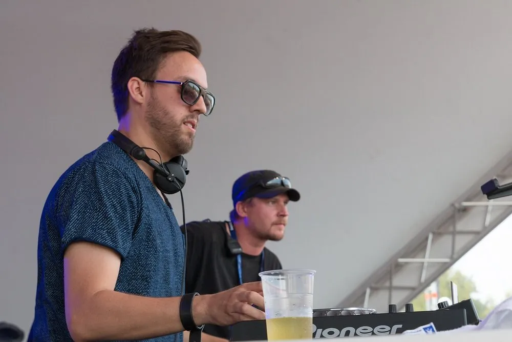 Maceo Plex pincha con gafas de sol y auriculares al cuello junto a otro DJ, bajo la carpa blanca de un escenario de festival