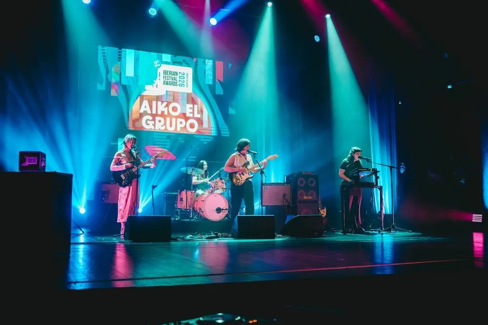 Aiko el Grupo toca con guitarras, teclado y batería en el escenario del Coliseu Micaelense, bajo focos azules y con el nombre de la banda en la pantalla del fondo, durante la gala de los Iberian Festival Awards 2026
