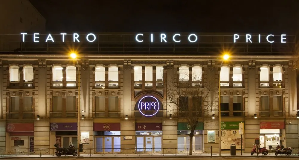 Fachada del Teatro Circo Price de Madrid de noche, con el rótulo iluminado sobre el edificio de ladrillo y el logotipo circular del Price en el centro