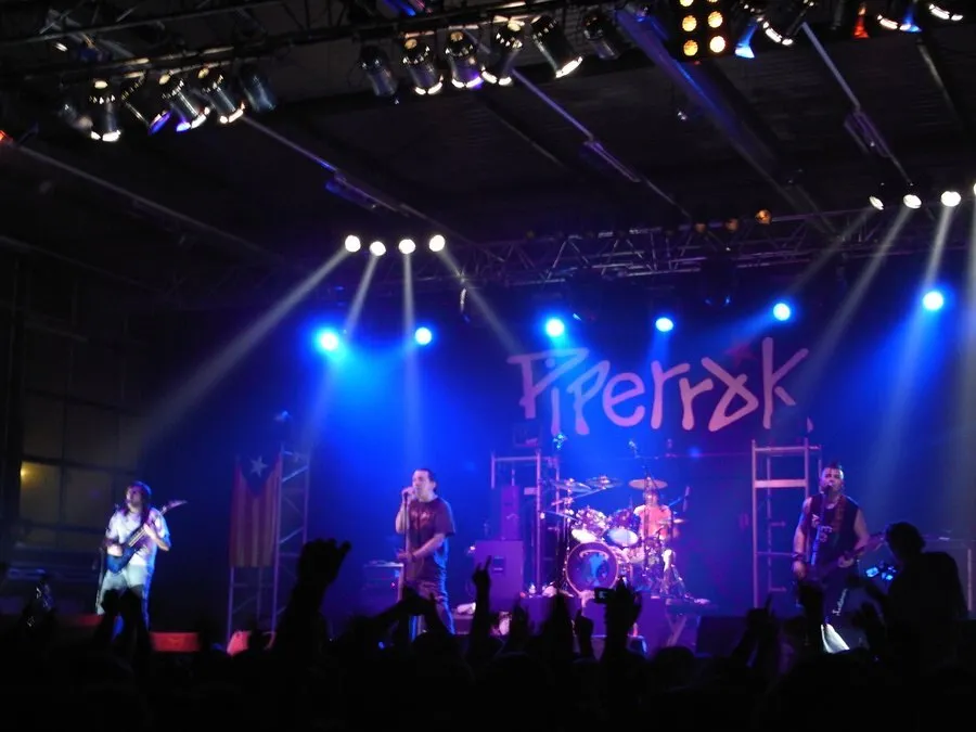 Concierto de Piperrak en un pabellón, con el nombre del grupo iluminado al fondo del escenario, el cantante en el centro y el público levantando los brazos en primer plano