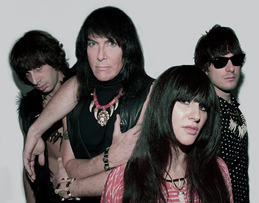 Retrato promocional de The Fuzztones: cuatro músicos con ropa oscura, collares de colmillos y gafas de sol posan ante un fondo blanco, con una mujer de flequillo negro en primer plano