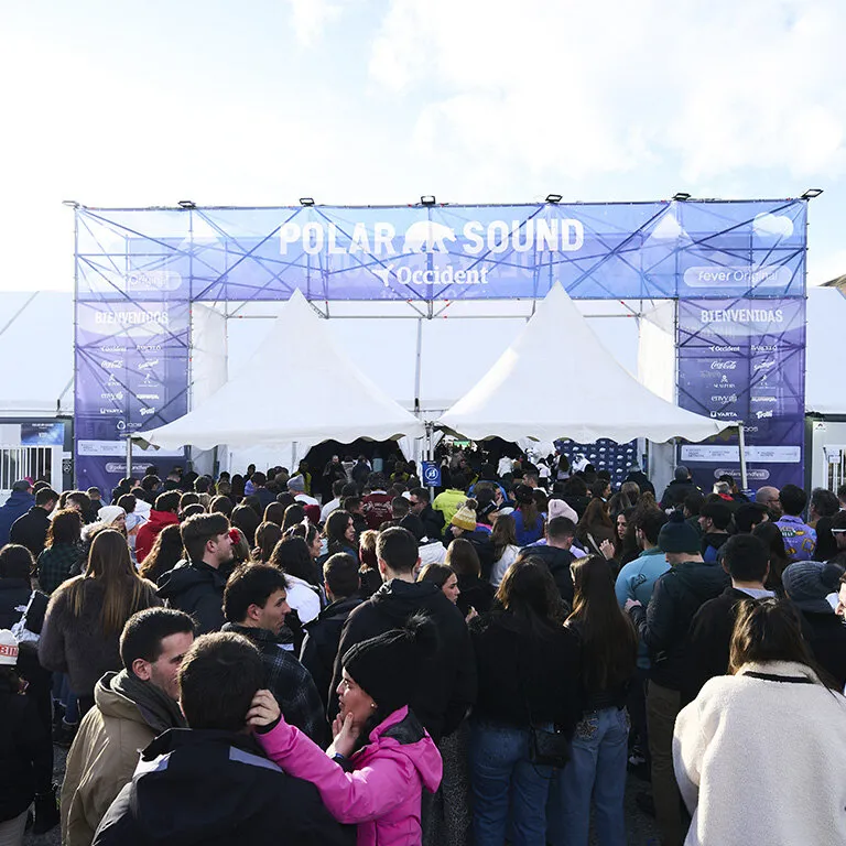 Wrapped-up crowd queuing under the Polar Sound entrance arch, with the festival logo, welcome signs and two white marquees behind