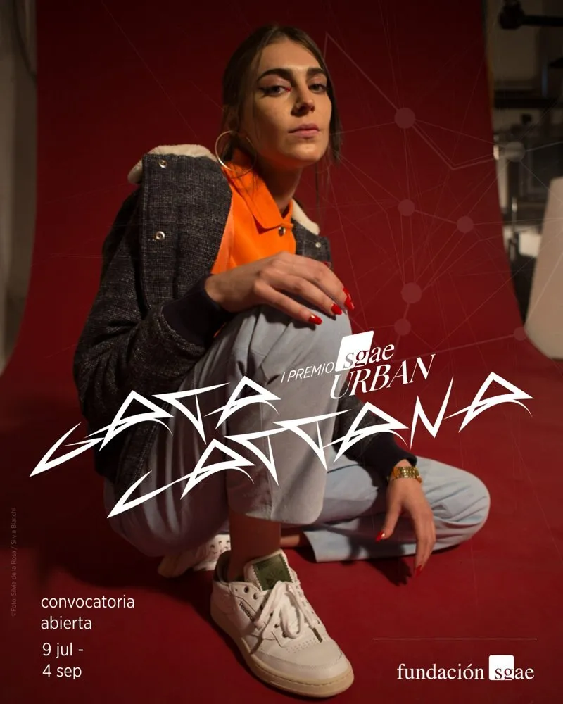 Poster for the call for entries of the 1st Premio SGAE Urban Gata Cattana: a woman crouching against a red fabric background, wearing a grey jacket, an orange polo shirt and white trainers, with the prize logo in white lettering
