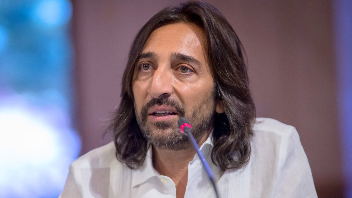 Antonio Carmona, con camisa blanca y el pelo largo, hablando ante un micrófono