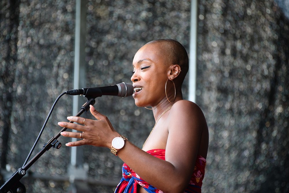 Dana Masters canta ante un micrófono con un pañuelo rojo y estampado durante un concierto al aire libre