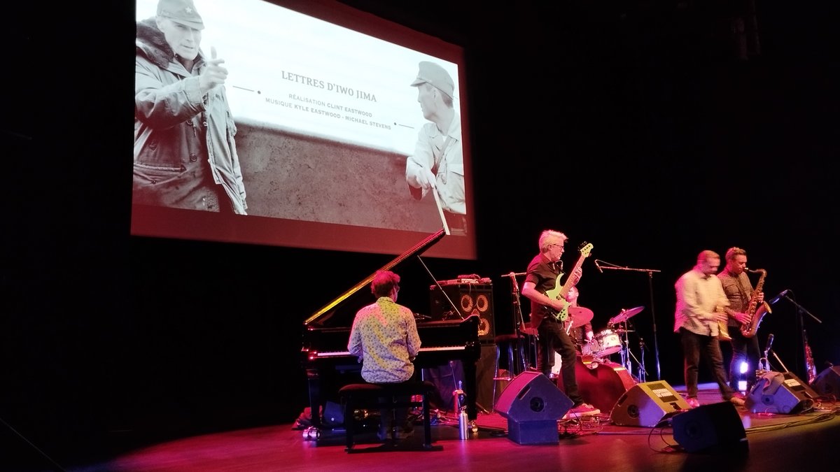 El quinteto de Kyle Eastwood toca en un escenario con piano, bajo y saxos bajo una pantalla con una imagen de Cartas desde Iwo Jima