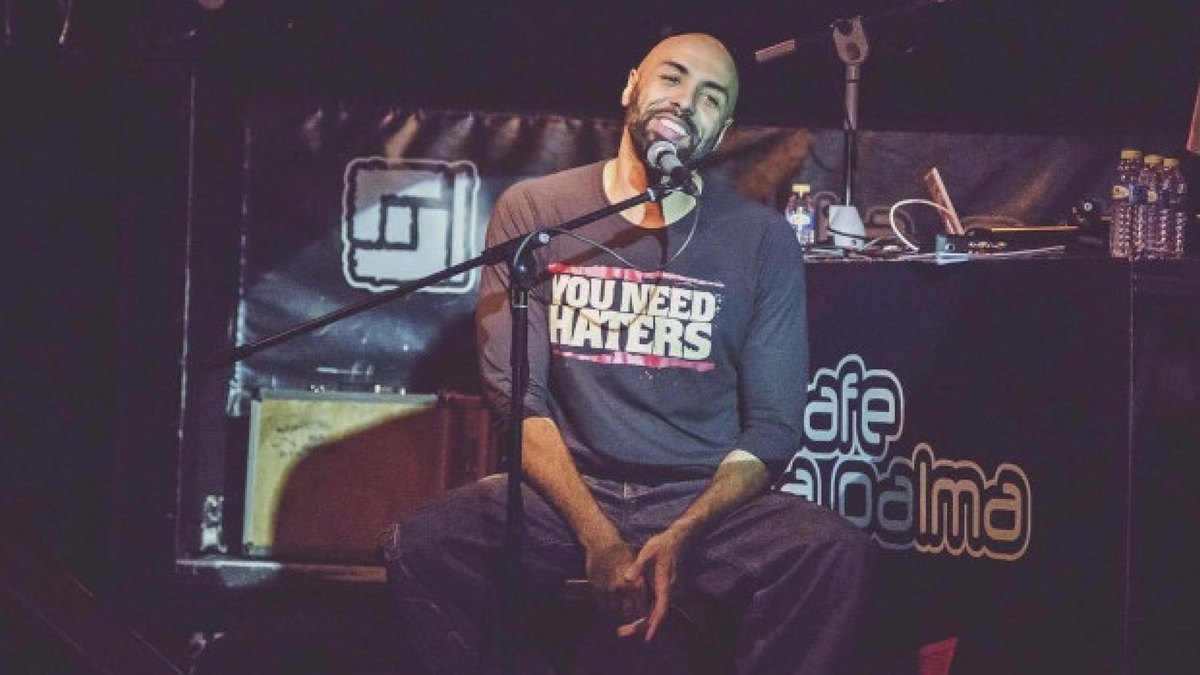 El Chojin canta sentado con el micrófono en un concierto en sala, en la imagen promocional del Madrid Urban Fest 2026
