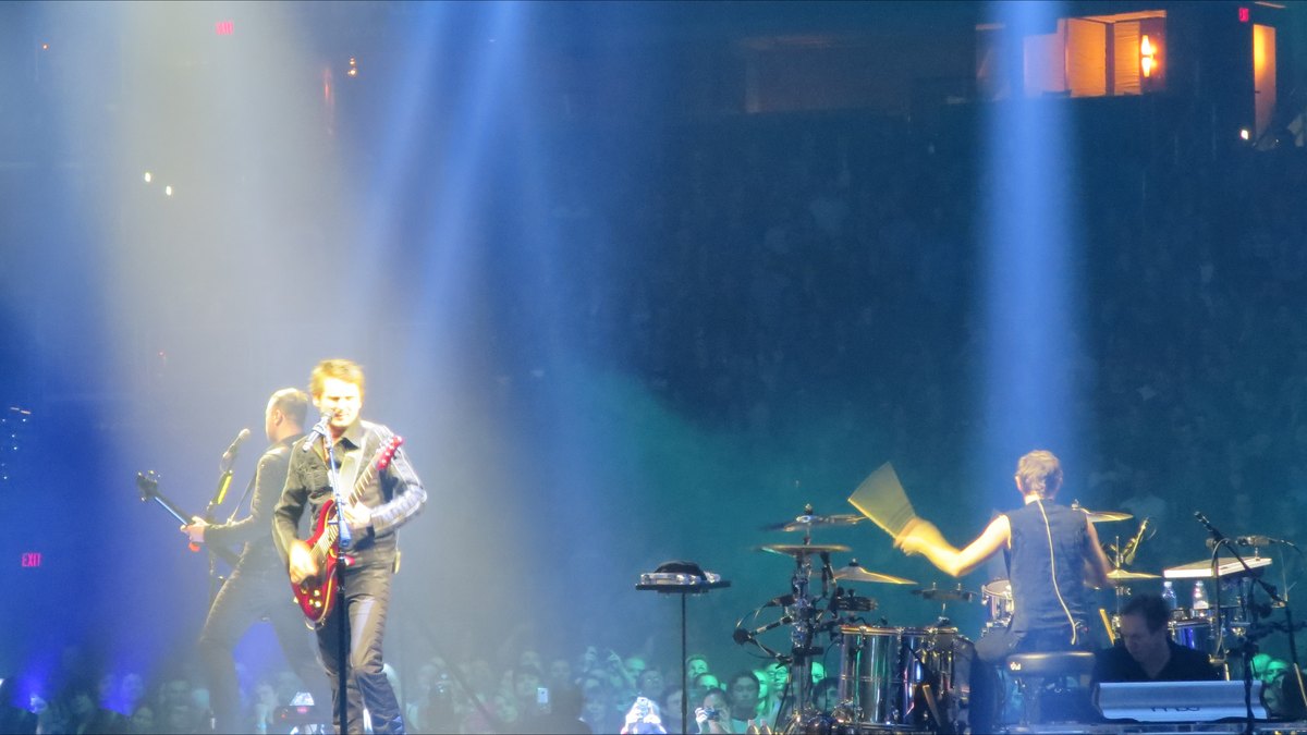 Muse en concierto con Matt Bellamy a la guitarra y la batería iluminada por focos azules