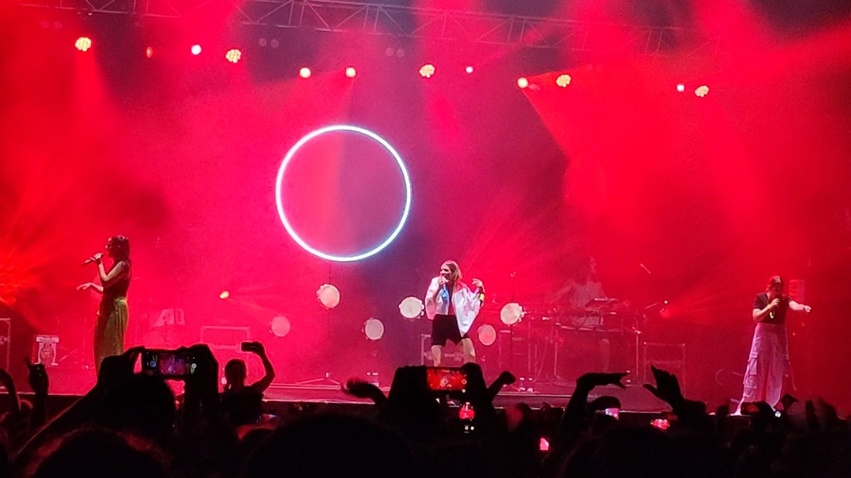 Tanxugueiras cantando sobre un escenario bañado en luz roja, con un aro luminoso al fondo y el público con los móviles en alto