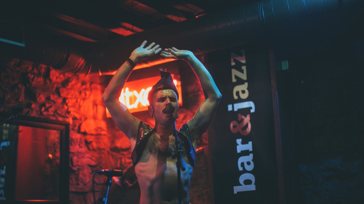 Rodrigo Cuevas actuando con los brazos en alto bajo una luz roja en un bar de conciertos