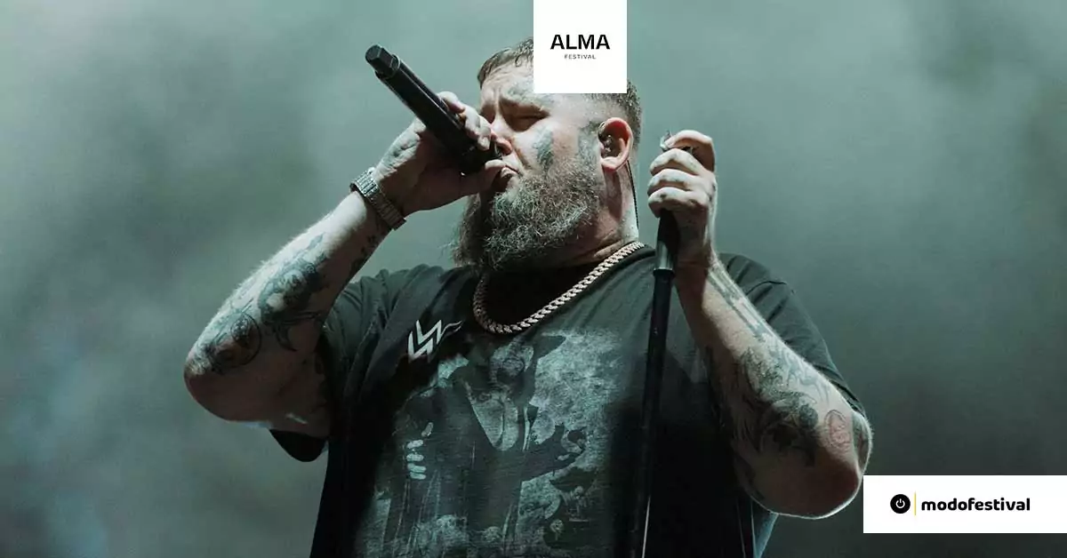 Rag’n’Bone Man cantando en vivo en Alma Occident Festival, con micrófono en mano y fondo iluminado.